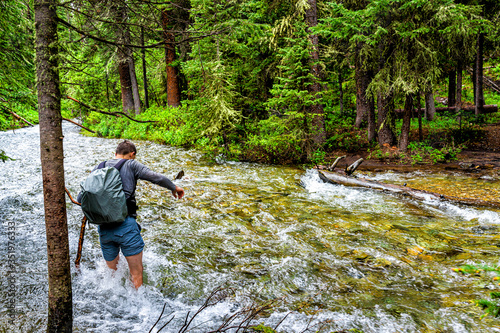 Man crossing fording river on Conundrum Creek Trail in Aspen, Colorado in 2019 summer in forest woods with strong current and deep water