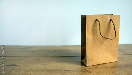 Disposable bag of kraft paper on a wooden table. Beautiful white background, copy space.