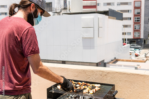 Man is barbequing in the terrace with a mask due covid 19