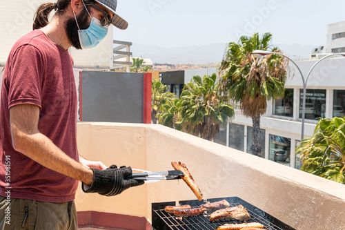 Man is barbequing in the terrace with a mask due covid 19