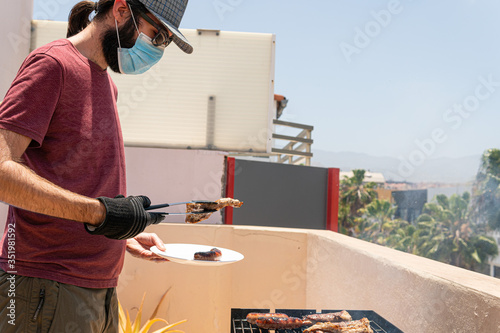 Man is barbequing in the terrace with a mask due covid 19