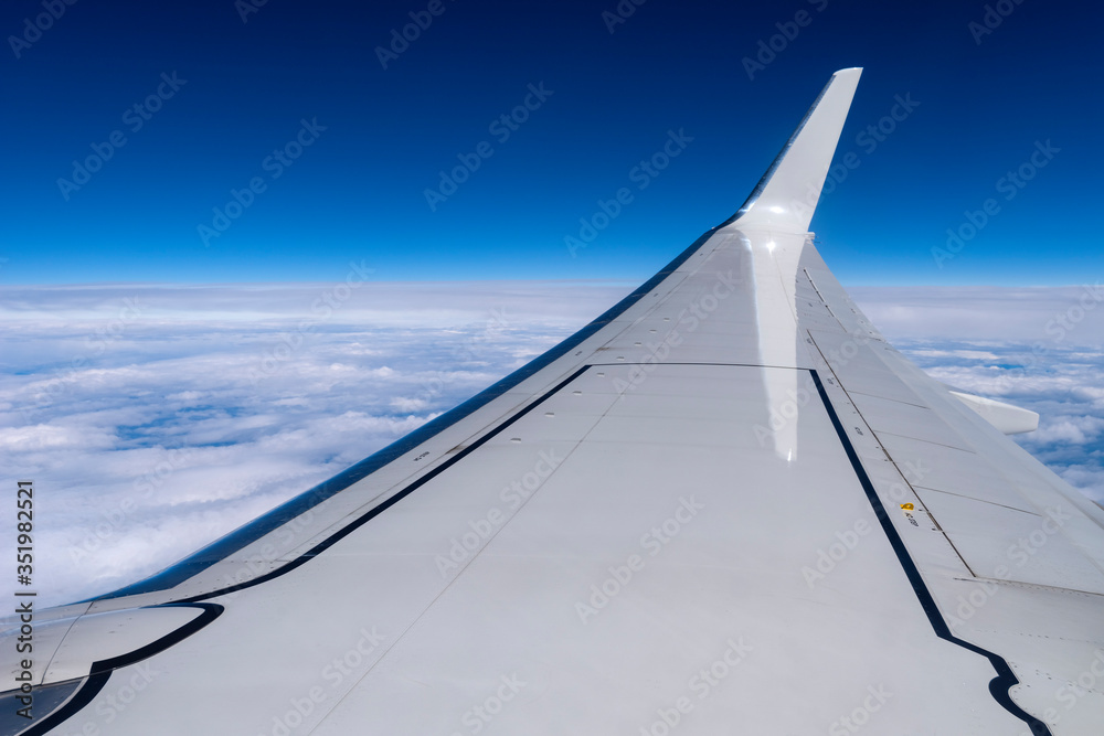 Wing of a flying airplane, blue sky and clouds.