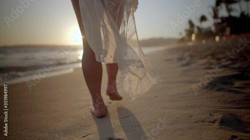 Young woman stands on beach as breeze blows through her hair and sun sets in the distance photo