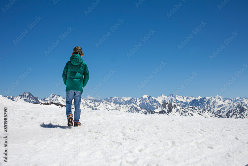 Boy walks in snowy mountatins with clear sky