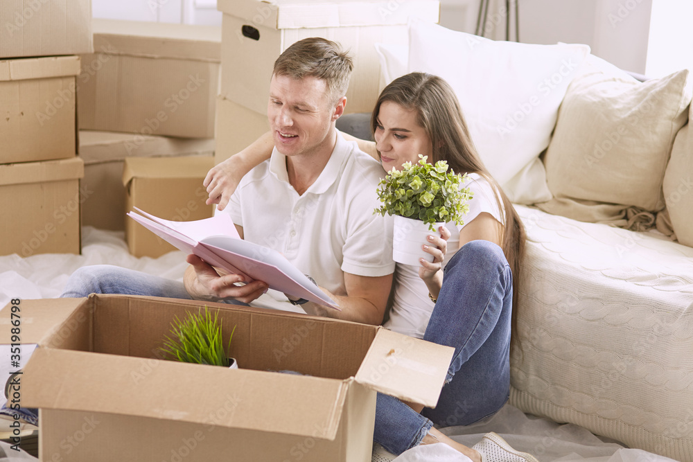 Portrait of happy couple looking at laptop computer together sitting in new house, surrounded with boxes Portrait of happy couple looking at laptop computer together sitting in new house, surrounded with boxes