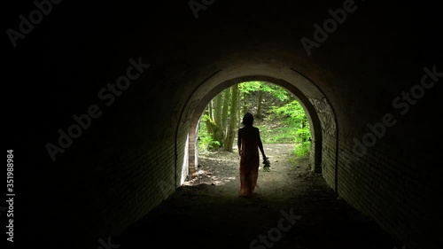 Girl in white dress with orange print comes out of the dark tunnel,rear view
