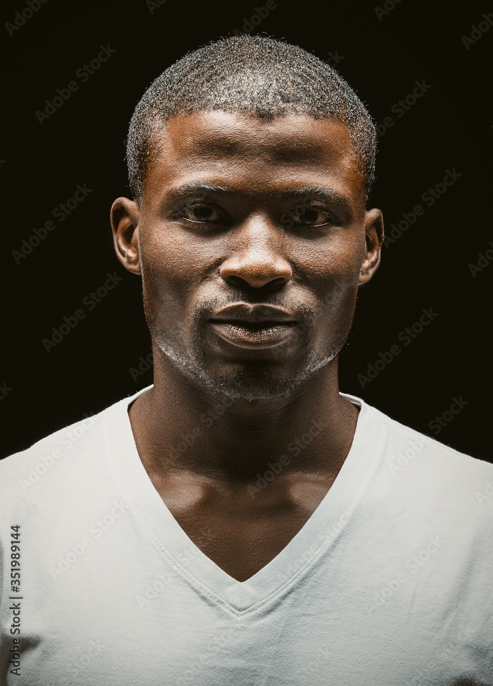 Confident Afro American man thoughtfully looking at camera. Serious attractive dark-skinned guy in a white t-shirt on black background. Toned image Confident Afro American man thoughtfully looking at camera. Serious attractive dark-skinned guy in a white t-shirt on black background. Toned image