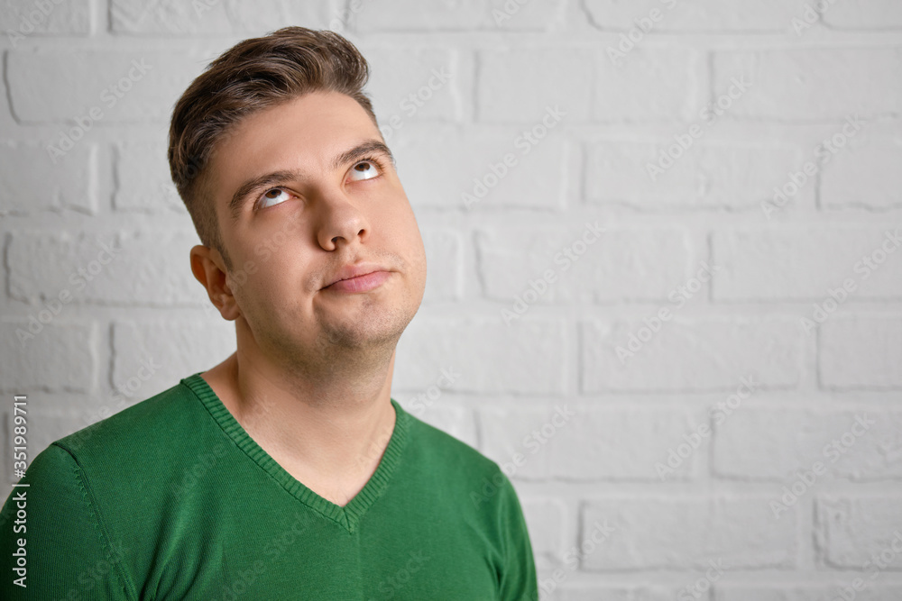 Confused rolls his eyes up, hands folded on his chest. Portrait of a handsome caucasian man. Brick wall background. Studio photo. Confused rolls his eyes up, hands folded on his chest. Portrait of a handsome caucasian man. Brick wall background. Studio photo.