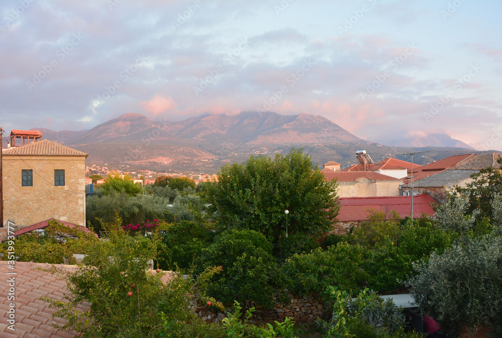 Gently pink sunset in a greek village. In the foreground are tiled roofs and green trees, a pomegranate bush. In the background the beautiful mountains of Peloponnese, Greece.