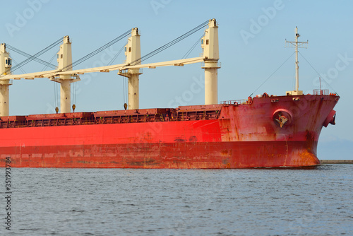 Large red bulk carrier (cargo ship) with a cranes sailing in an open sea from Europoort. Clear blue sky with cirrus clouds. Rotterdam, Netherlands. Global communications, logistics, industry theme photo