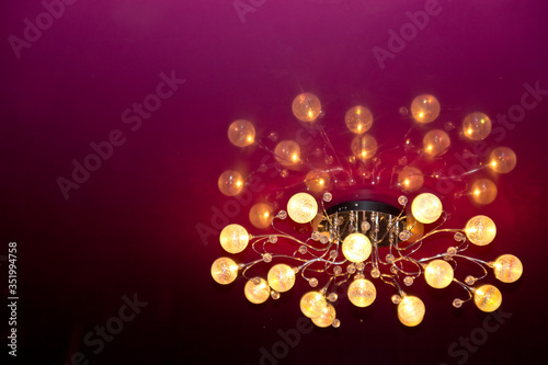 The chandelier on the red ceiling. Balls on the chandelier.Burning light bulbs. View from below. Homeliness.