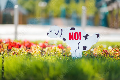 Dog warning sign. Sign in the form of a pooping dalmatin dog, with the inscription NO. Installed on a green lawn with flowers, prohibiting walking dogs photo