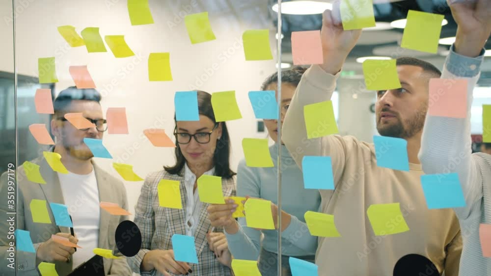 Slow motion of male and female coworkers working with colorful sticky notes brainstorming planning business in office. Meetings and job concept.