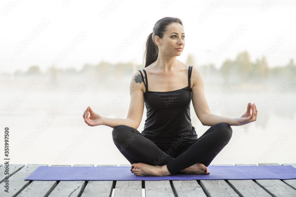 Young woman practicing yoga outdoors. Harmony and meditation concept. Healthy lifestyle. Beautiful girl sits in a pose of a half lotus near the lake, she practicing yoga meditation. Kundalini energy