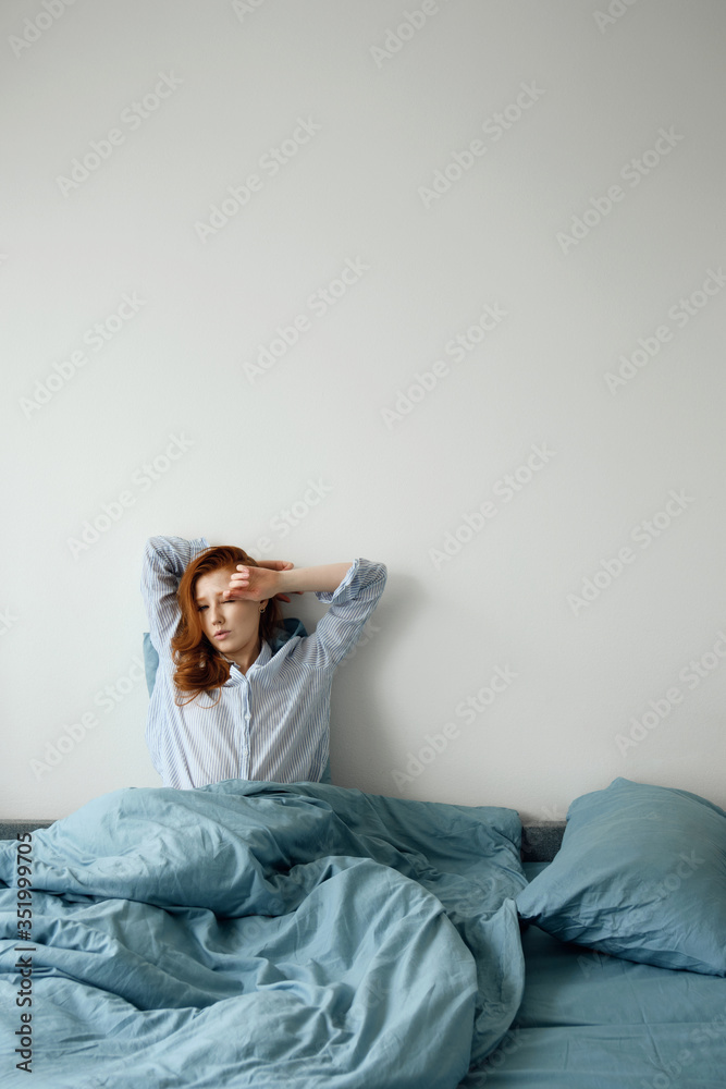 The red-haired girl sits in a blue bed with her back against a white wall, throwing her hands to her head. Empty space on top. The red-haired girl sits in a blue bed with her back against a white wall, throwing her hands to her head. Empty space on top.