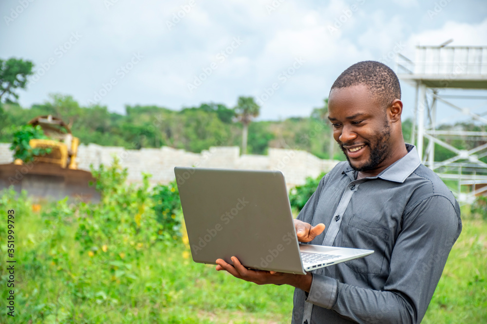 young african agricultural businessman, using a laptop on a plot of land young african agricultural businessman, using a laptop on a plot of land