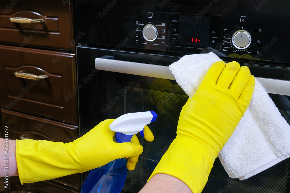 Cleaning service in the kitchen. Hands in gloves, washing and cleaning a gas stove in the kitchen with a rag.