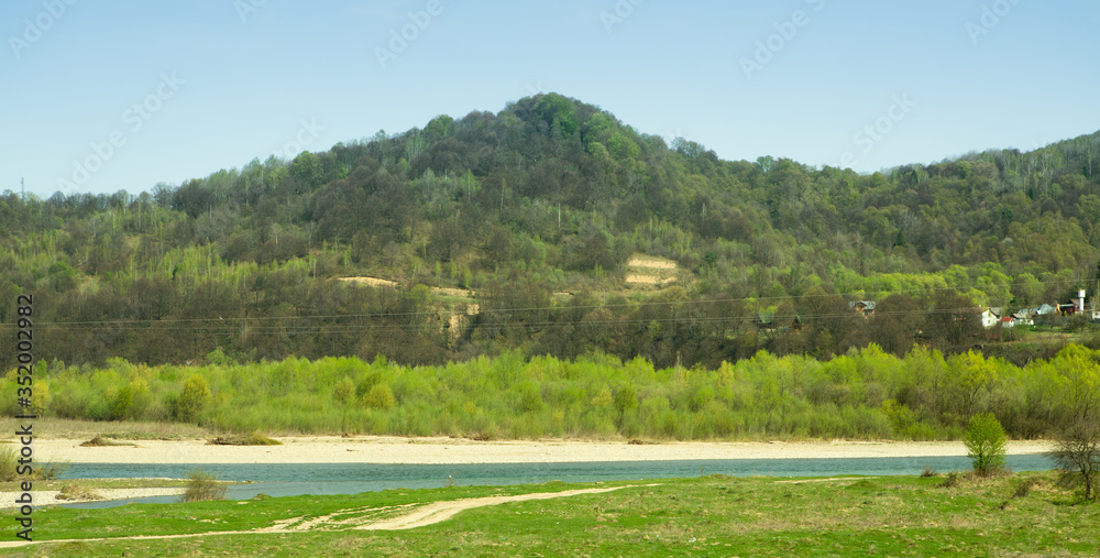 Mountain landscape river village. Beautiful landscape on warm summer or spring day. Mountain covered with deciduous forest, river with sandy beach and cottage village