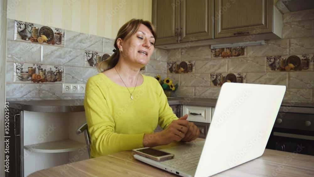 Young caucasian smiling woman with laptop communicates in online chat and social networks while at home in the kitchen. The blogger conducts live broadcasts for his followers. Home leisure. Young caucasian smiling woman with laptop communicates in online chat and social networks while at home in the kitchen. The blogger conducts live broadcasts for his followers. Home leisure.