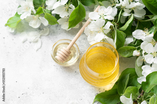 Obraz na płótnie Flower honey in a glass jar on the background of flowering branches. Liquid honey in a glass jar on a light gray table. Jar of honey close-up. Top view with space for text w salonie