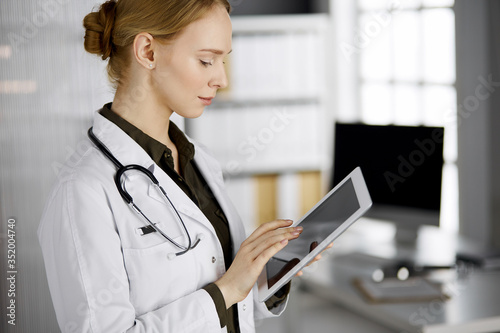 Friendly smiling female doctor using tablet computer in clinic. Perfect medical service in hospital. Medicine concept
