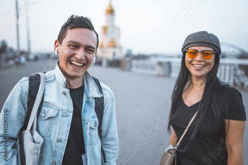 Couple of tourists with suitcase on embankment of river. Happy man and woman laughs looking at the camera. Wanderlusting concept photo