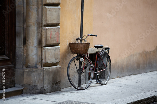 Bicycle standing near wall of ancient building. Female bike with wicker basket in front is fastened with chain to post on street of European city. Wallpaper or background. Copy space at right side