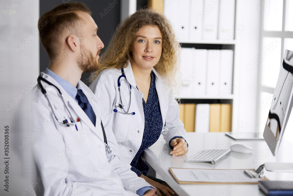 Red-bearded doctor with female colleague discussing current disease therapy while sitting at working place in clinic. Team work in medicine Red-bearded doctor with female colleague discussing current disease therapy while sitting at working place in clinic. Team work in medicine