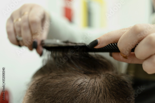 the man sits and he is cut. a man's haircut. women's hands of a hairdresser. scissors, comb, hair. neat haircut. process of trimming a person. © Илья Антропов