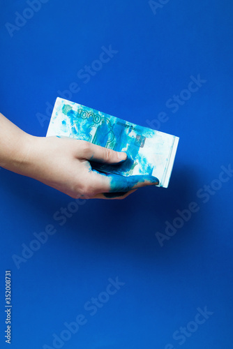 Concept : two hand holds few Russian banknotes - 1000 rubles - covered by blue paint on a blue background