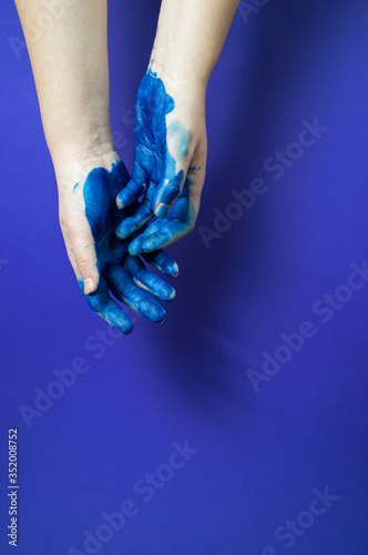 Two hands of artist in bright blue paint on blue background