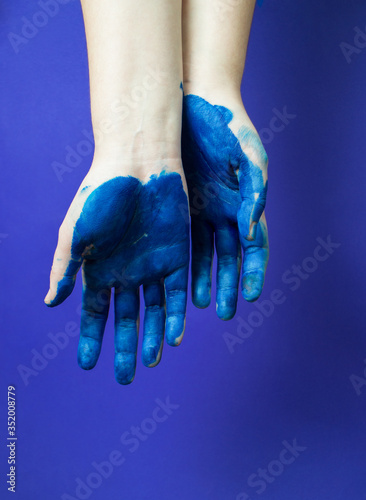 Two hands of artist in bright blue paint on blue background