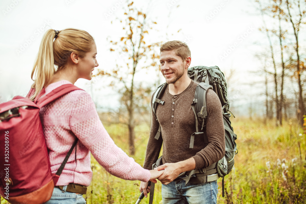 Romantic date for couple of backpackers in wild nature. Happy man and women looks each other holding hands while standing against background of autumn field. Hiking concept. Adventure concept