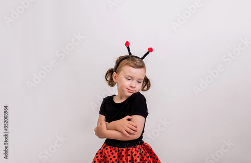 Portrait of a little girl hugging herself in a ladybug costume on a white isolated background with space for text