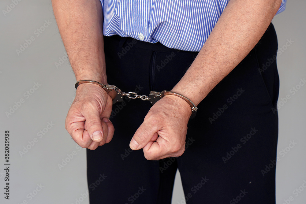 Prisoner or arrested caucasian terrorist, closeup of hands in handcuffs. Arrested elderly man handcuffed hands isolated on gray background.