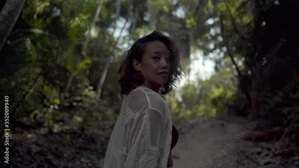 Mysterious attractive woman walks through jungle forest wearing long flowing dress inviting viewer to come along with her Mysterious attractive woman walks through jungle forest wearing long flowing dress inviting viewer to come along with her