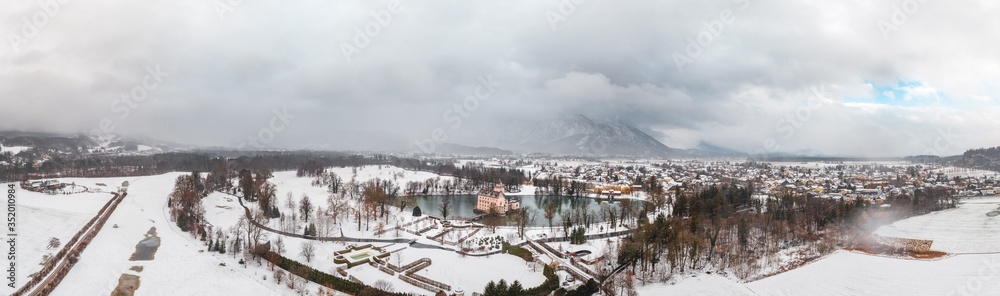 Panoramic aerial view of Schloss Anif moated in artificial pond at Salzburg outskirts in heavy snow during winter view of untersberg snow mountain