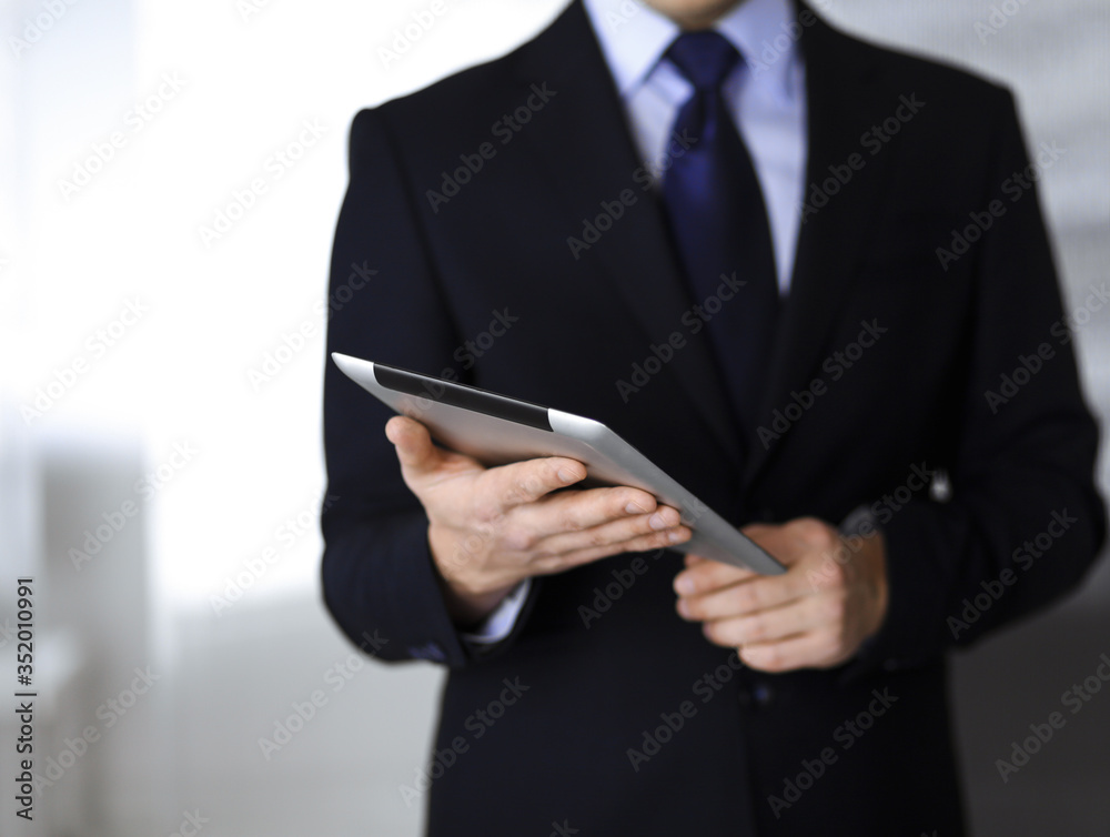 Business people use a tablet computer for discussion of their new project, standing in a modern office. Unknown businessman or male entrepreneur with a colleague at workplace. Teamwork and partnership Business people use a tablet computer for discussion of their new project, standing in a modern office. Unknown businessman or male entrepreneur with a colleague at workplace. Teamwork and partnership