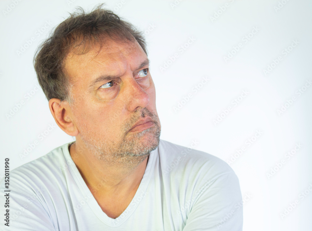 Middle-aged man with white T-shirt and quarantined boredom. Altered concentration and tiredness at home office. Middle-aged man with white T-shirt and quarantined boredom. Altered concentration and tiredness at home office.