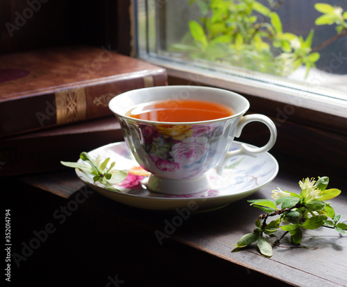 Cup of tea with blooming twig and books near window