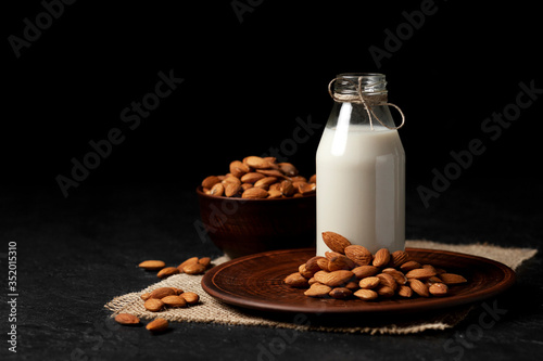 one bottle of almond milk on a dark black background with nuts, vegetarian milk without sugar and lactose
