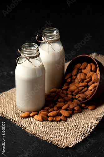 almond milk in bottles with nuts on a dark black table, a variety of dairy products without sugar and lactose, a vegetarian drink