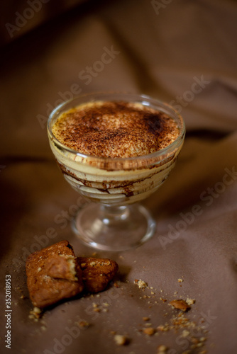 classic tiramisu cake in a beautiful glass form on a brown background, food photo, sweetness, festive dessert