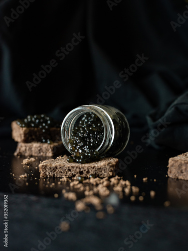 food photo glass jar of black caviar fish sturgeon on slice of dark bread