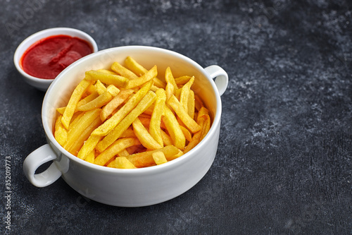 French fries with barbecue sauce, in a white bowl, against a dark background with place for text.