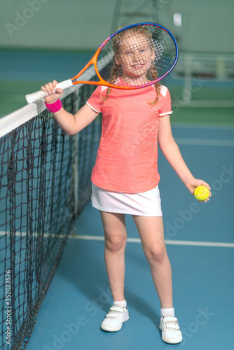A happy playful girl smiles mischievously on the tennis court with a racket. © sheikoevgeniya