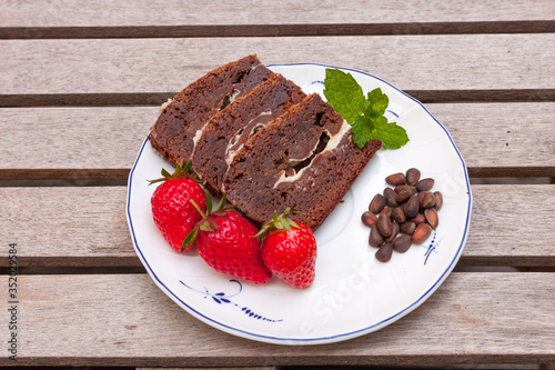 Brownie coffee cake decorated with strawberries and mint on a wooden table.