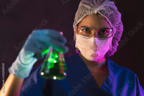 Nurse wearing hazmat suit,  protective goggles and antiviral mask kn95 for covid19, dark room laboratory performs virus or antidote scan using surgical glove holding blood and coronavirus test sample