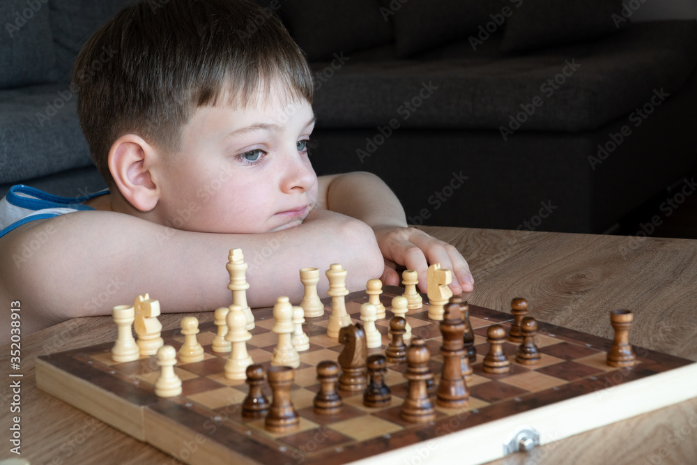 The serious child lost in thought playing chess. Playing board games, on coronavirus quarantine. The child playing chess.
