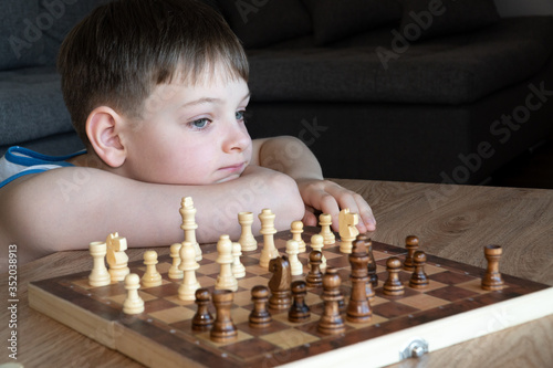 Obraz na płótnie The serious child lost in thought playing chess. Playing board games, on coronavirus quarantine. The child playing chess. w salonie